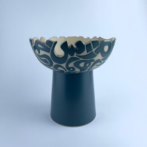 An elevated bowl with featuring a scalloped rim cut with flowing calligraphy motifs