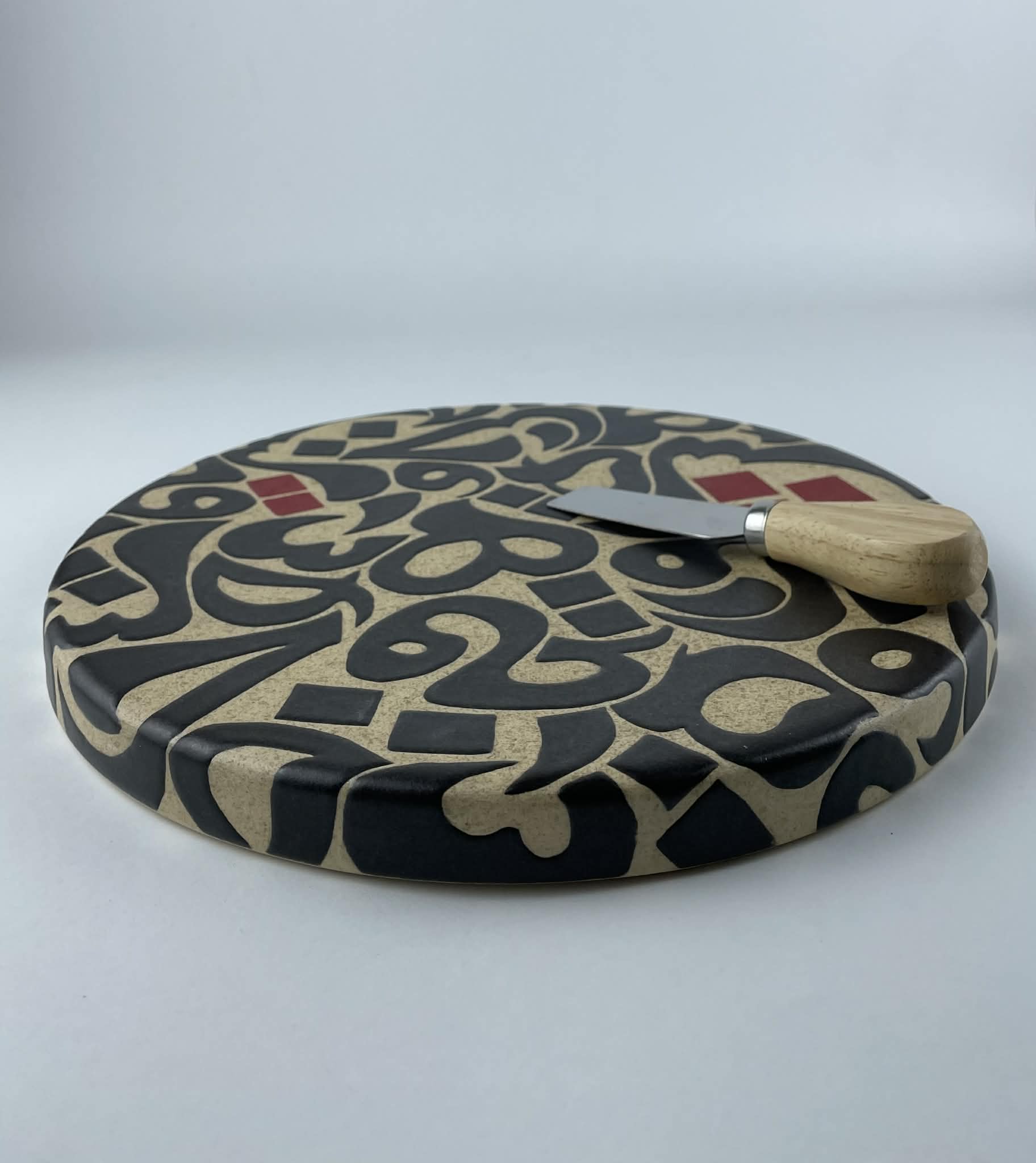 A cylindricalical cheese platter featuring a calligraphic design with flowing black forms