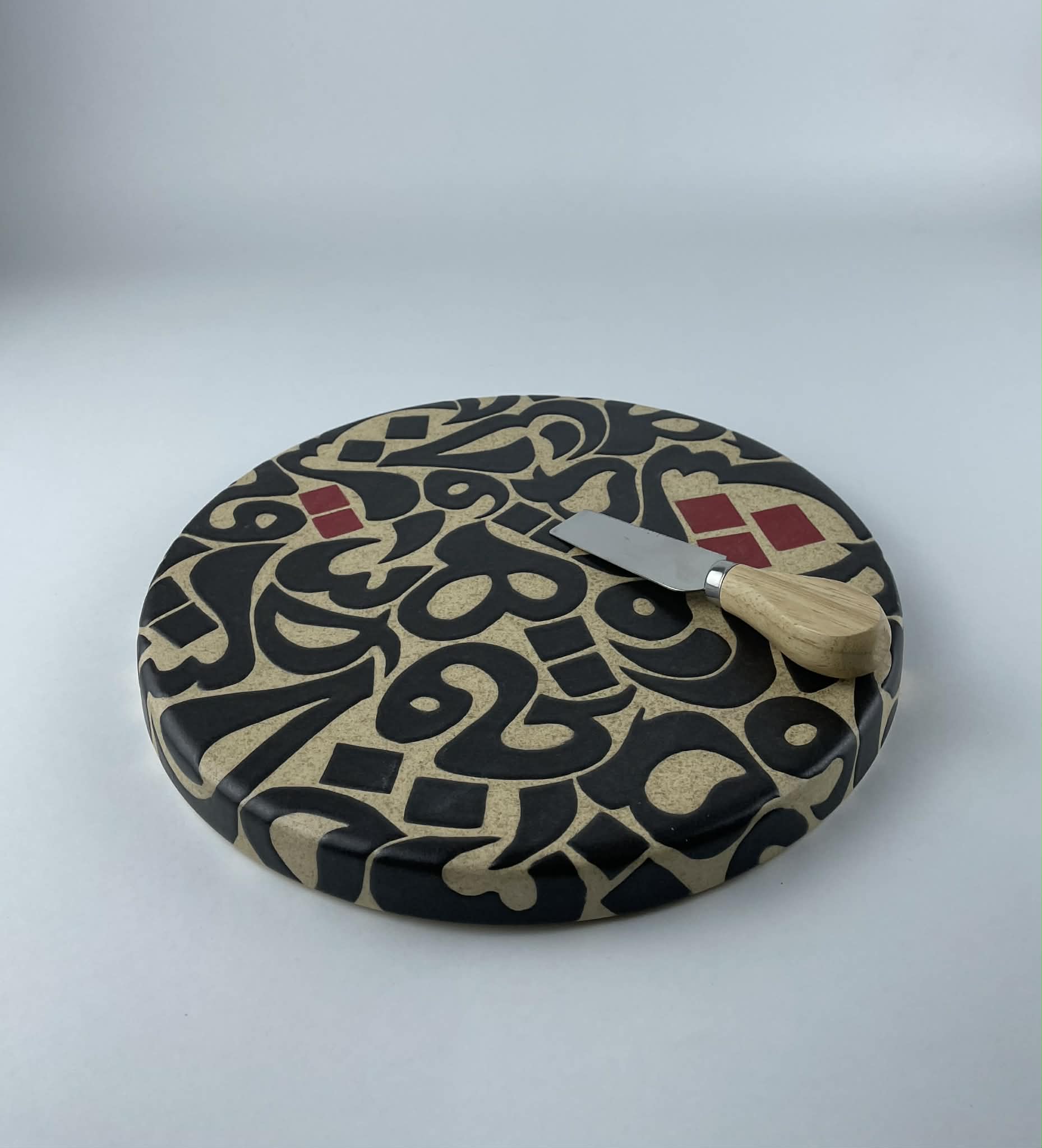 A cylindricalical cheese platter featuring a calligraphic design with flowing black forms