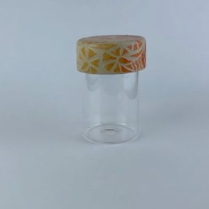 A clear glass storage container topped with a handcrafted cylindrical ceramic bowl finished with an ombré effect