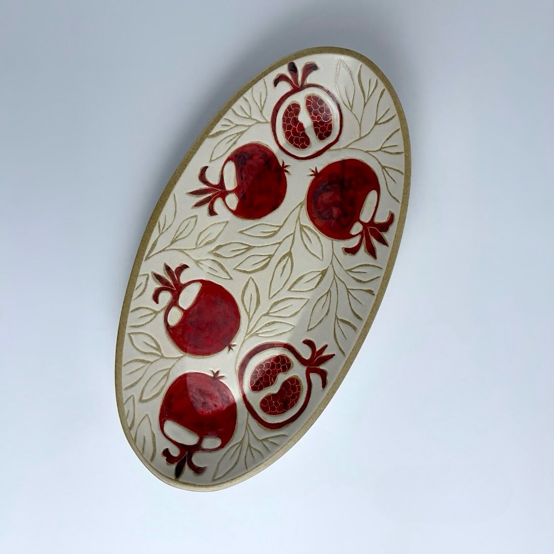 A tapered oval plate featuring red pomegranate motifs. Suitable for serving food