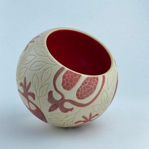 A ball-shaped bowl adorned with pomegranate motifs and a glossy red interior. Designed for serving and display.