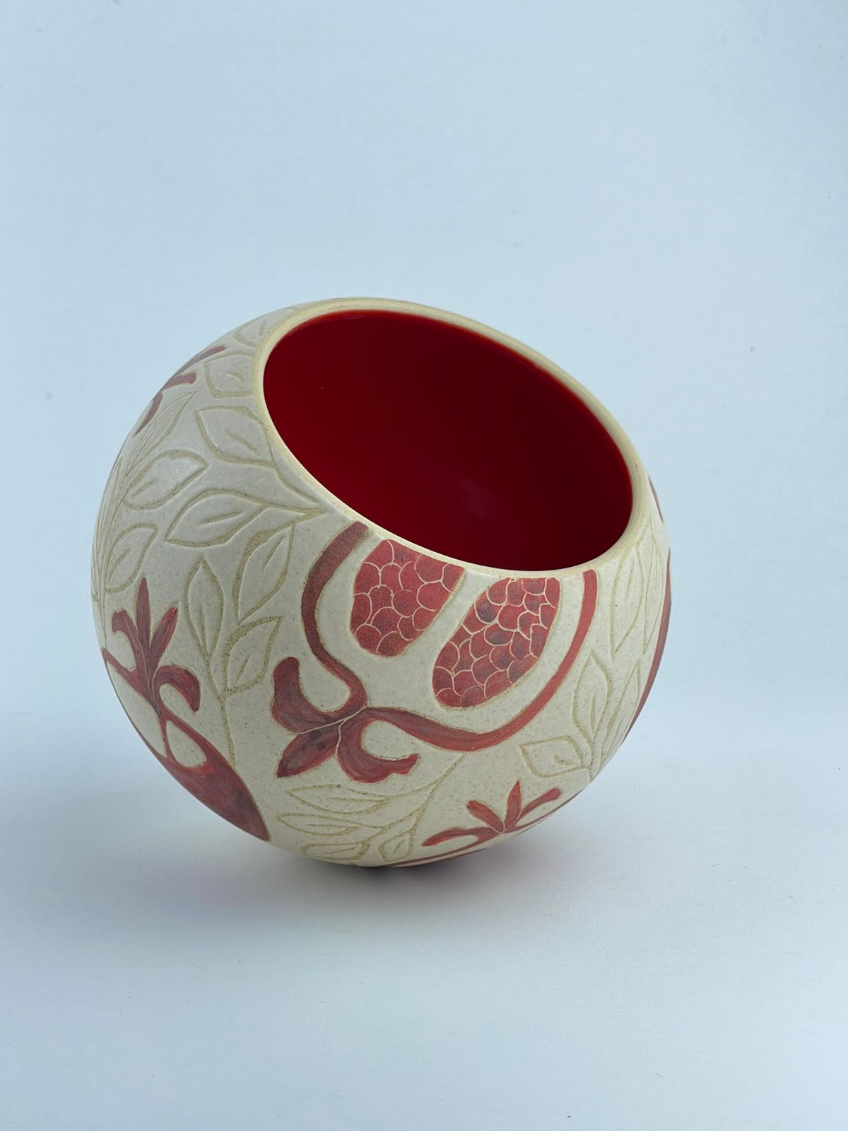 A ball-shaped bowl adorned with pomegranate motifs and a glossy red interior. Designed for serving and display.