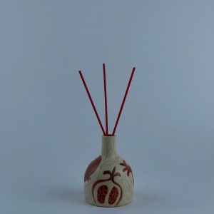 A reed diffuser featuring pomegranate motifs with a red interior. Designed for use with fragrance reeds.