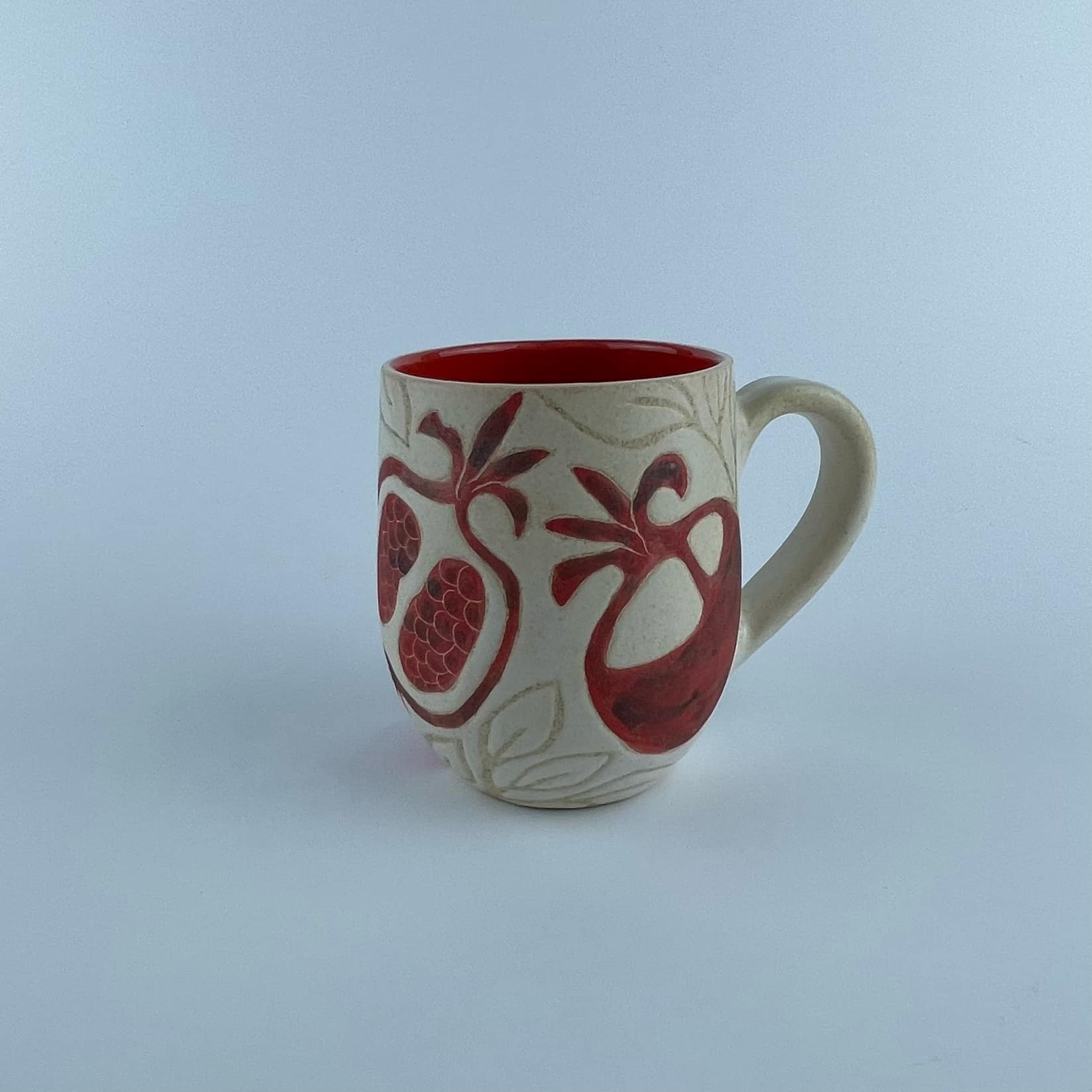 A U-shaped mug featuring a red pomegranate motifs for serving coffee and beverages.